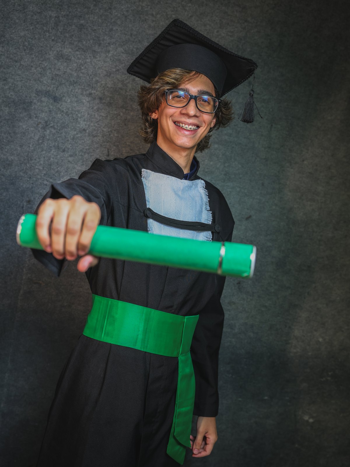 Caio de beca e capelo segurando o canudo do diploma